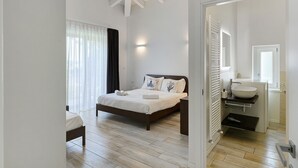 Quarto com cama, mesa de cabeceira e banheiro com pia e espelho.