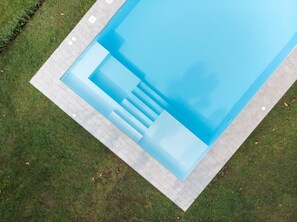 En vy från ovan av en rektangulär swimmingpool med en kant av kakel och trappsteg som leder ner i vattnet.