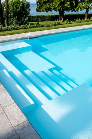 A swimming pool with clear blue water, surrounded by a tiled deck and greenery. - Apartment 'Flora' with Lake View, Wi-Fi and Air Conditioning (Garda)