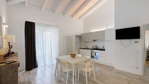 Uma cozinha moderna com armários brancos, um espaço de refeições com mesa e cadeiras brancas, e uma televisão de tela plana fixada na parede.