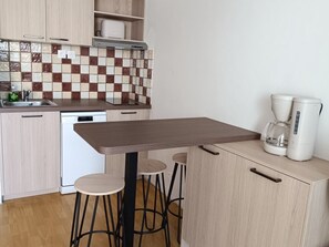 Eine kleine Küche mit Fliesenrückwand, einer Kaffeemaschine und einem Essplatz mit Hocker.