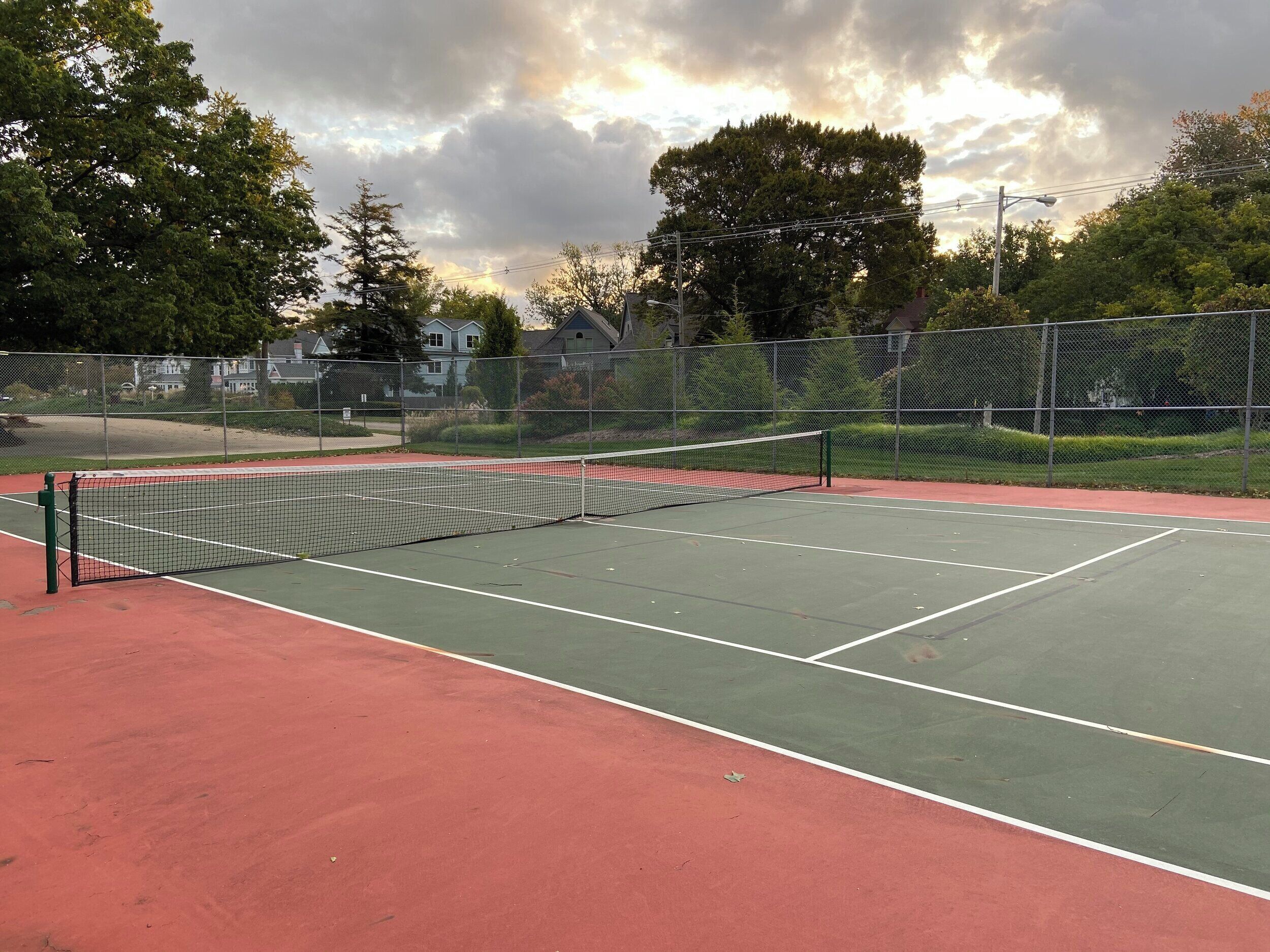 A tennis court with a net, surrounded by a fence and trees.