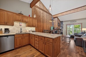 A kitchen with wooden cabinets, a dishwasher, and a stone fireplace. - Spacious, renovated 2 bedroom, vaulted ceilings, private deck (Winter Park)