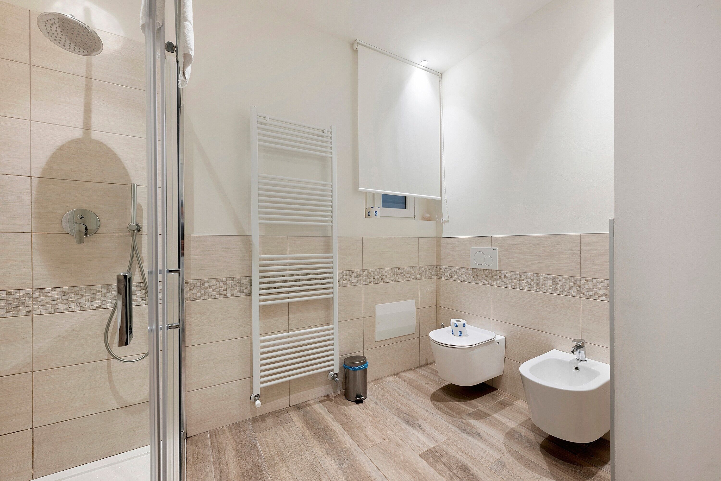Un baño moderno con cabina de ducha de vidrio, inodoro blanco, bidet y un pequeño cubo de basura.