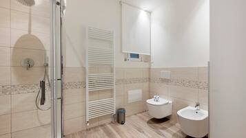 Un baño moderno con cabina de ducha de vidrio, inodoro blanco, bidet y un pequeño cubo de basura.