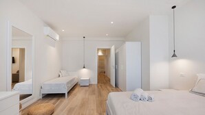 A modern hotel room with a large bed, two smaller beds, a wardrobe, a mirror, a bedside table, and a hanging light fixture. - Apartment 'Matilde' with Lake View, Wi-Fi and Air Conditioning (Garda)