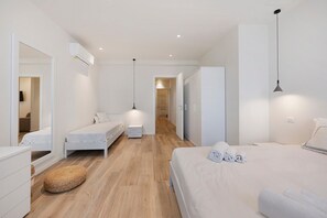 Une chambre d’hôtel moderne avec un grand lit, deux petits lits, une armoire, un miroir, une table de chevet et un luminaire suspendu.