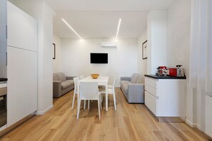 A modern kitchen with white cabinetry, a dining table with chairs, a flat-screen TV mounted on the wall, and a small kitchenette area. - Apartment 'Matilde' with Lake View, Wi-Fi and Air Conditioning (Garda)
