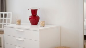 A white bedside table with a red vase and two glass candle holders. - Apartment 'Matilde' with Lake View, Wi-Fi and Air Conditioning (Garda)
