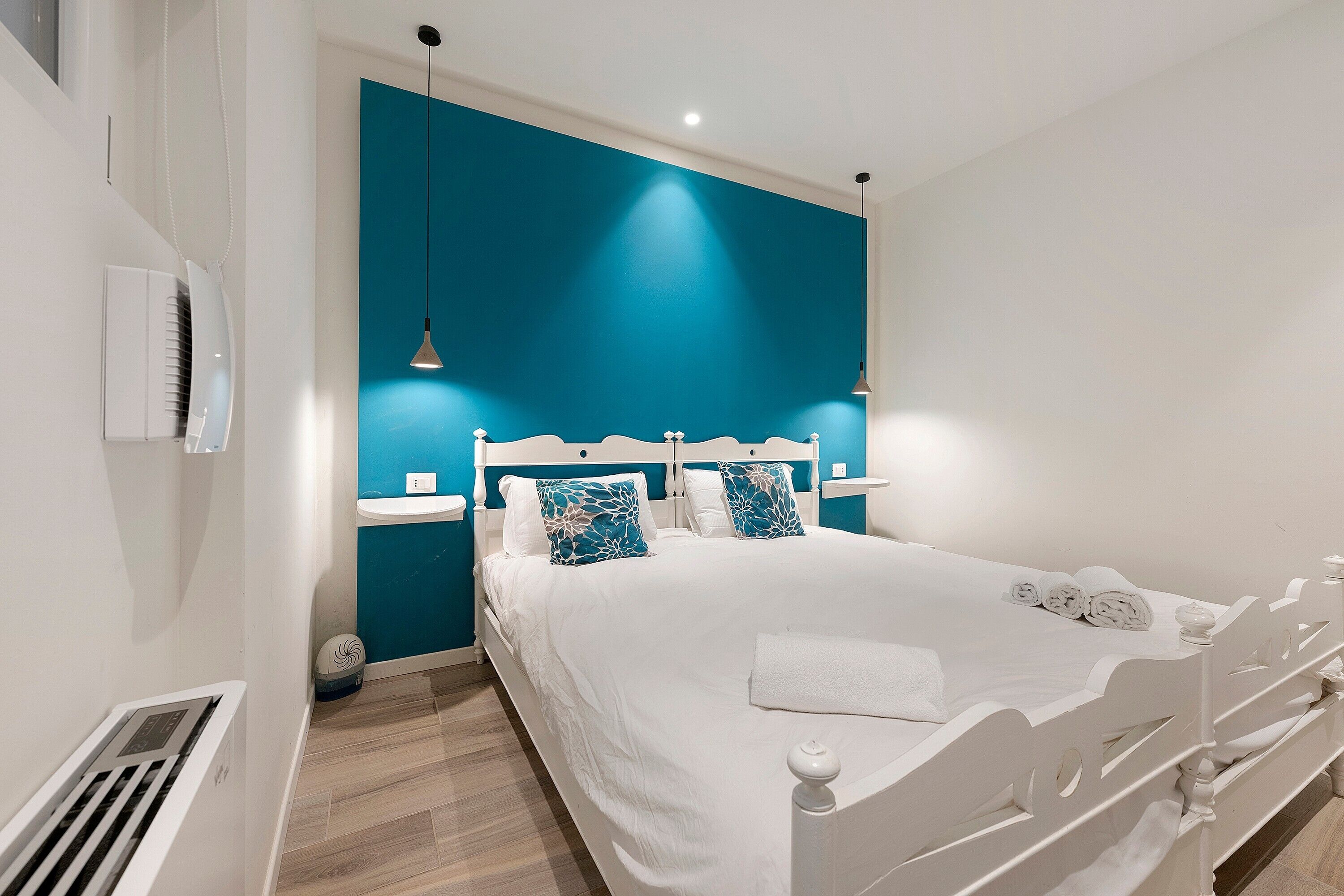 Ein modernes Schlafzimmer mit einem weißen Bett, einer Türkis-farbenen Akzentwand und einem weißen Nachttisch.
