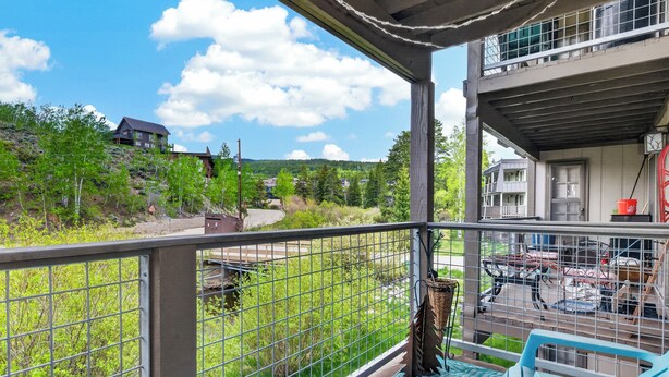 Een balkon met uitzicht op een groen landschap, een eethoek met tuinmeubilair, en een gebouw met een balkon.