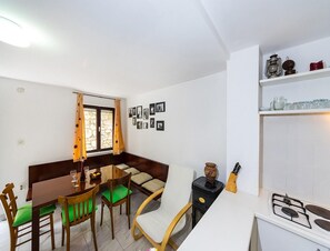 Ein Essbereich mit Tisch und Stühlen, einem Fenster mit Vorhängen, einem Herd und einem Regal mit Küchenutensilien.
