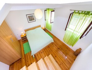 Ein Schlafzimmer mit einem Bett, Nachttischlampen, einem grünen Teppich, einem hölzernen Kleiderschrank, einem gerahmten Bild und einer Pendelleuchte.