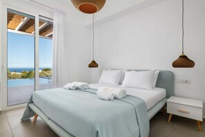 Ein Schlafzimmer mit einem Bett, zwei Nachttischen, Meerblick und einem großen Fenster.