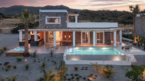 Ein modernes Haus mit Steinfassade, einem Swimmingpool und einer Terrasse mit Gartenmöbeln.