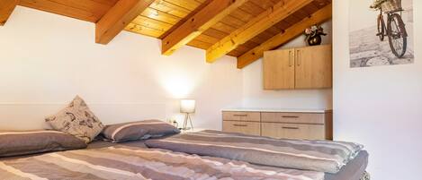 A bedroom with a wooden ceiling, a bed with striped bedding, a nightstand with a lamp, and a wall-mounted cabinet.
