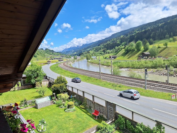 A view of a road curving alongside a river, with a bridge and a house in the foreground.