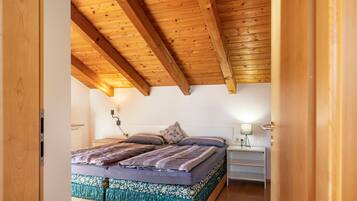 Ein Schlafzimmer mit Holzboden, einem Bett mit gemusterten Betttextilien, einem Nachttisch mit Lampe und einem Beistelltisch.