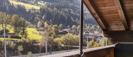 A wooden balcony with a view of a valley, houses, and a mountain in the background.