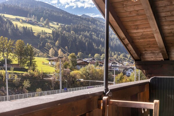 A wooden balcony with a view of a valley, houses, and a mountain in the background.