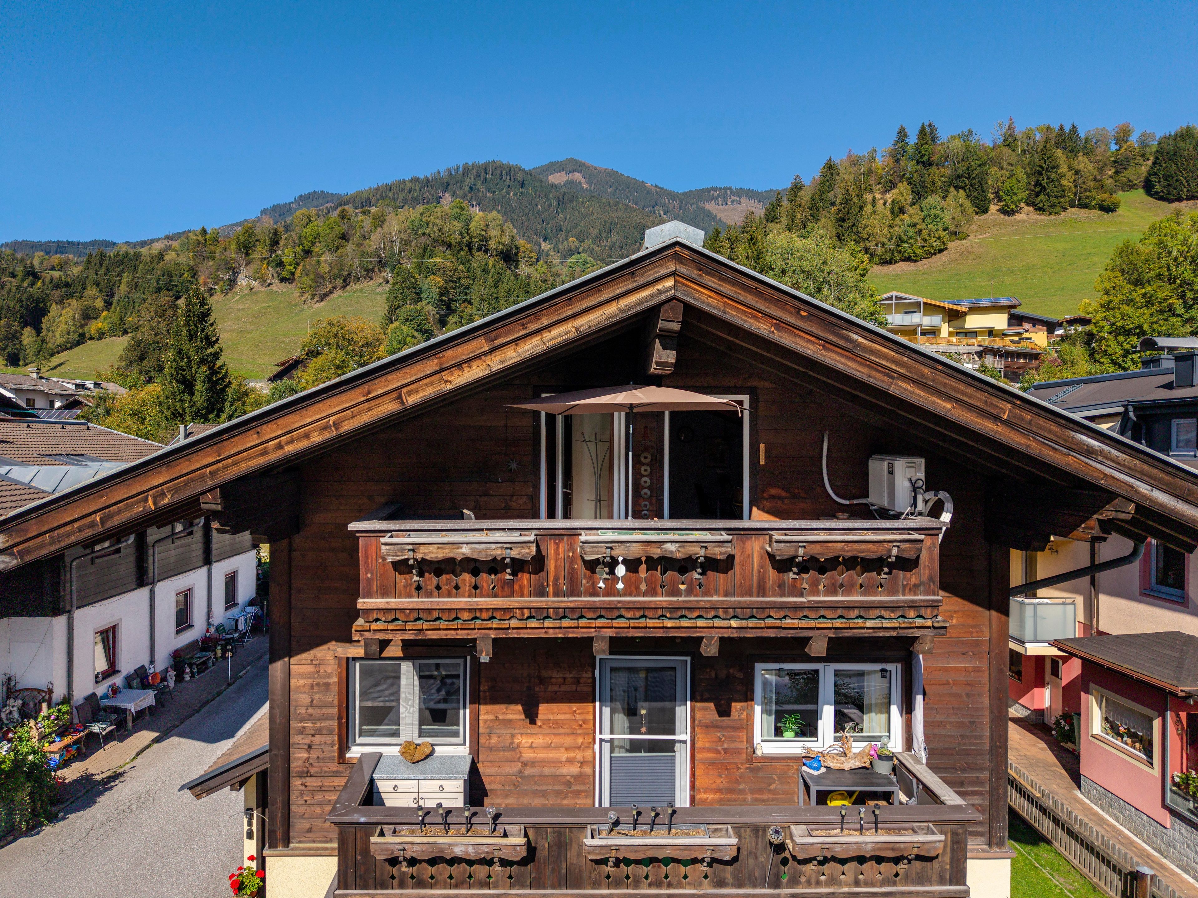 A wooden chalet with a balcony, large windows, and a view of a mountainous landscape.