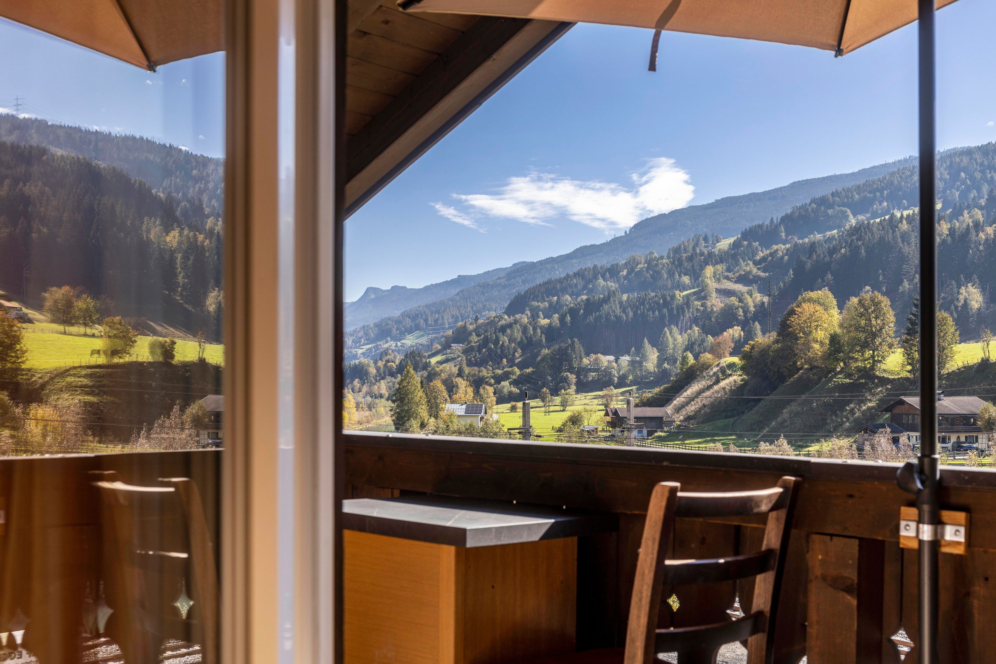 A view from a balcony with a table and chairs, overlooking a valley with mountains and a clear sky.