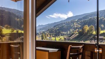 A view from a balcony with a table and chairs, overlooking a valley with mountains and a clear sky.