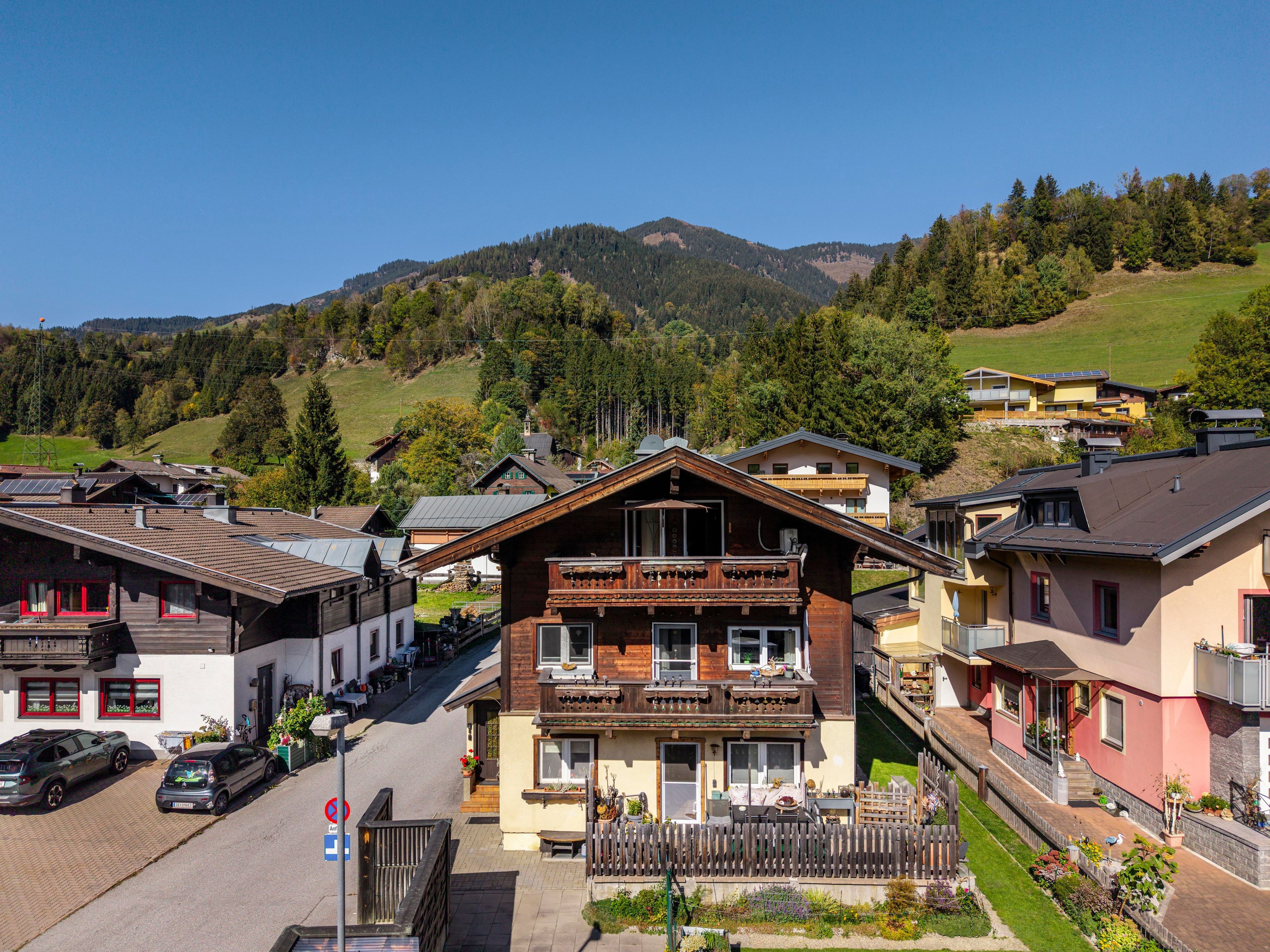 Eine Bergstadt mit traditionellen Holzhäusern, eine Straße mit geparkten Autos und Blick auf die umliegenden Hügel.