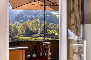A wooden-framed window with a view of a forested hillside and a clear sky.