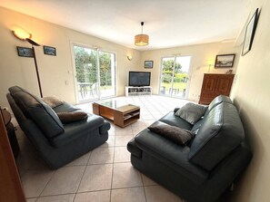 A living room with two leather sofas, a coffee table, a TV, and a sliding glass door leading to an outdoor area. - Large house with parking - 9 guests (Trégastel)