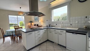 Une cuisine avec des meubles blancs, un lave-vaisselle encastré, une fenêtre avec vue et un coin repas comprenant une table et des chaises.