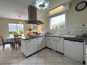 A kitchen with white cabinets, a built-in dishwasher, a window with a view, and a dining area with a table and chairs. - Large house with parking - 9 guests (Trégastel)
