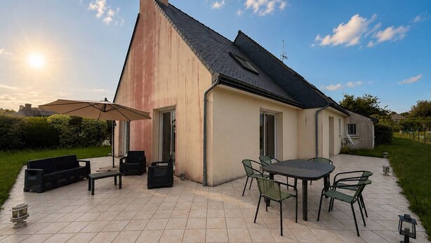 Une maison avec un patio carrelé, du mobilier d’extérieur et un grand parasol.