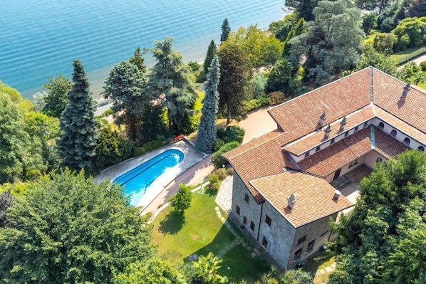 An aerial view of a property with a swimming pool, lush greenery, and a building with a tiled roof.