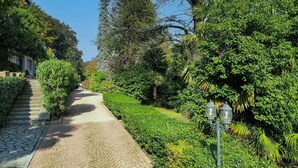 A paved pathway flanked by lush greenery and a building on the left. - Luxury Lakeside Retreat with a Pool near Stresa! Lake Maggiore Villa Romanza (Stresa)