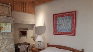 Ein Schlafzimmer mit einem hölzernen Bett, einem Nachttisch mit Lampe, einem Sessel, einer Steinwand und einem gerahmten Zertifikat.