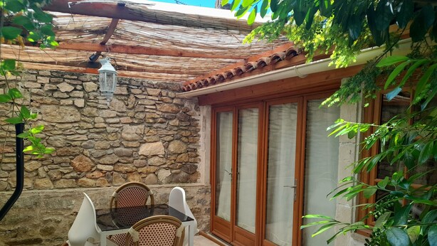 Eine Terrasse mit einer Steinmauer, einem Ziegeldach und einer Holztür mit Glasscheiben.