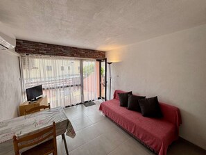 Ein Zimmer mit einer roten Couch, einem Fernseher auf einem Holztisch und einem gemusterten Vorhang.