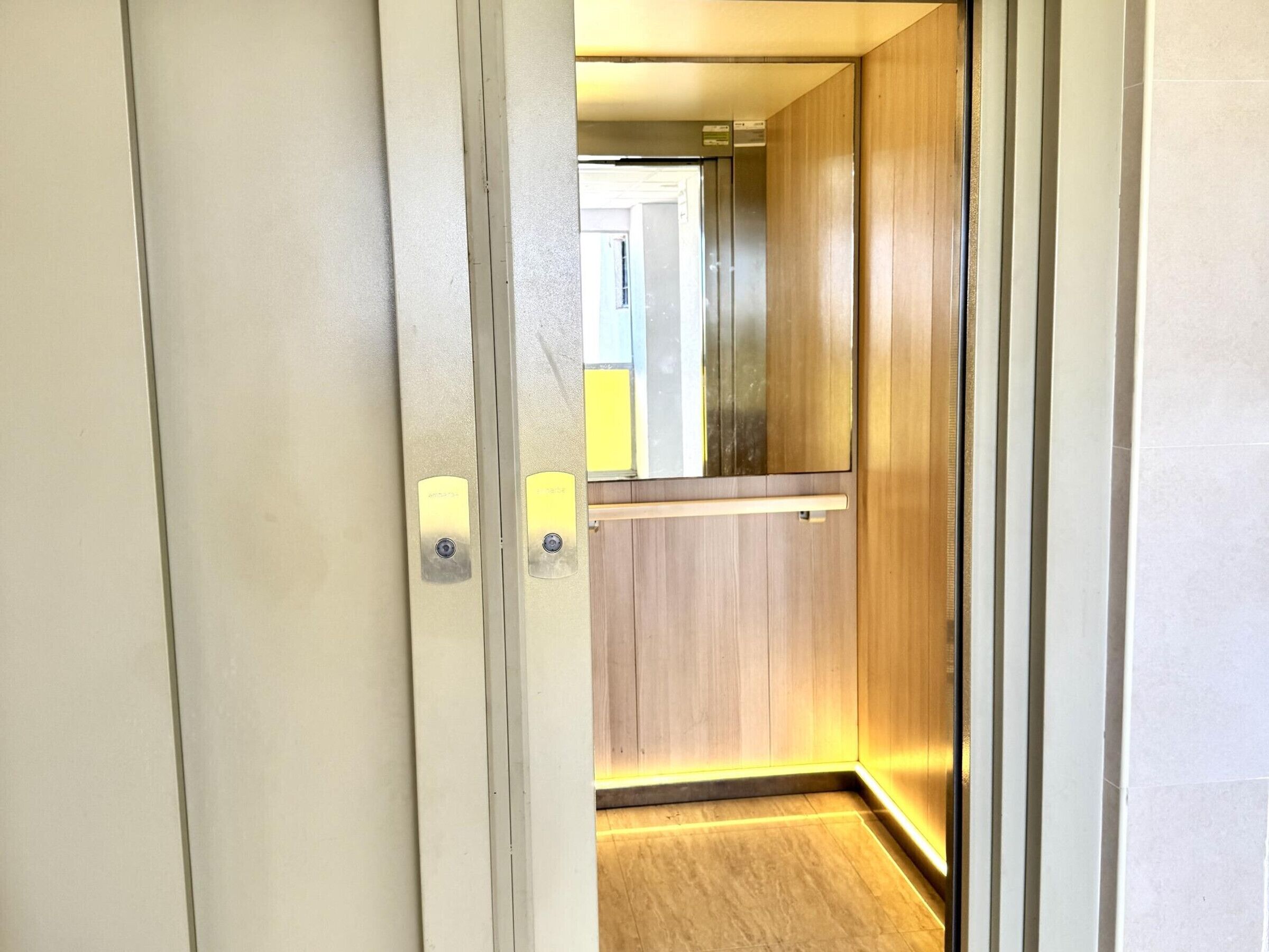 Vista del interior de un pasillo con una puerta de madera, un interruptor de luz y un aplique en la pared.