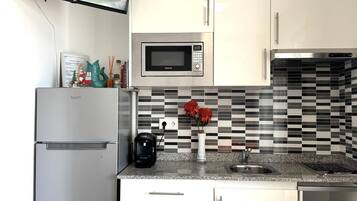 Una cocina con armarios blancos, microondas, cafetera y salpicadero de azulejos.