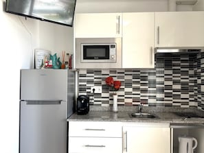 Una cocina con armarios blancos, microondas, cafetera y salpicadero de azulejos.