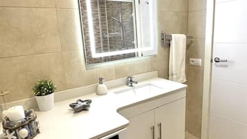 A bathroom with a white sink, a mirror, a shower, and a door.