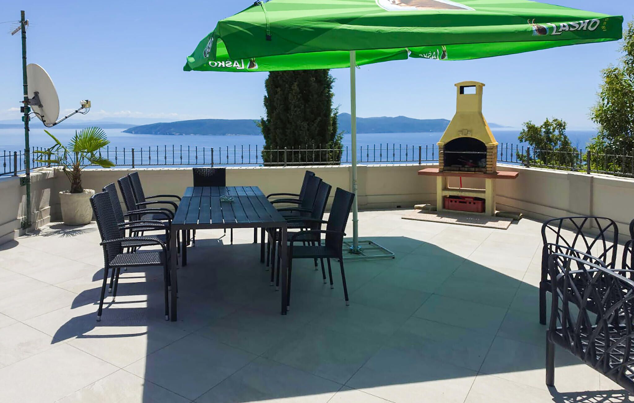 A terrace with a table and chairs, a green umbrella, a satellite dish, and a brick oven.