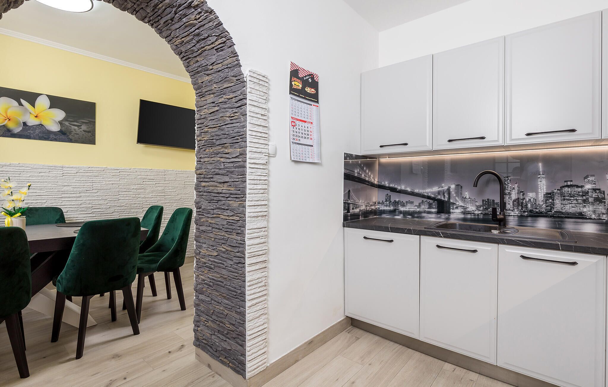 A modern kitchen with white cabinets, a stone accent wall, and a cityscape view.