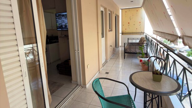 Un balcón con mesa y sillas, una puerta corrediza y una cocina visible a través de la puerta.