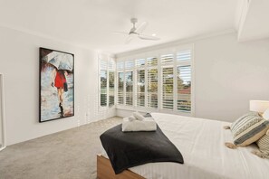 Ein Schlafzimmer mit Bett, Deckenventilator, Fenster mit Jalousien und einem Bild an der Wand.