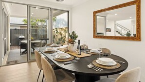 Un comedor con una mesa grande dispuesta para seis personas, un espejo en la pared y un ventanal corredizo que da a un espacio exterior.