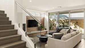 Un salon moderne avec un escalier, un téléviseur à écran plat, un canapé et une table basse.