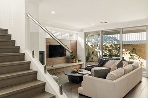 Un salon moderne avec un escalier, un téléviseur à écran plat, un canapé et une table basse.