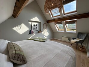 Ein Schlafzimmer mit einem großen Bett, Oberlichtern, einem Sessel und einem Traumfänger an der Wand.